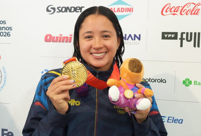 Nadadora colombiana sonriente muestra su medalla de oro y mascota oficial de los Juegos Suramericanos 2026, con cabello mojado tras competencia.